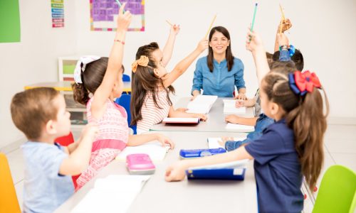 Group of preschool students raising their hands during class and trying to participate