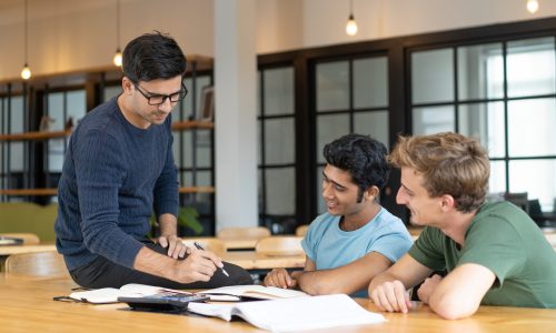 Serious teacher checking assignment of two students. Serious man in glasses pointing pen at notes of two cheerful guys. Education and internship concept
